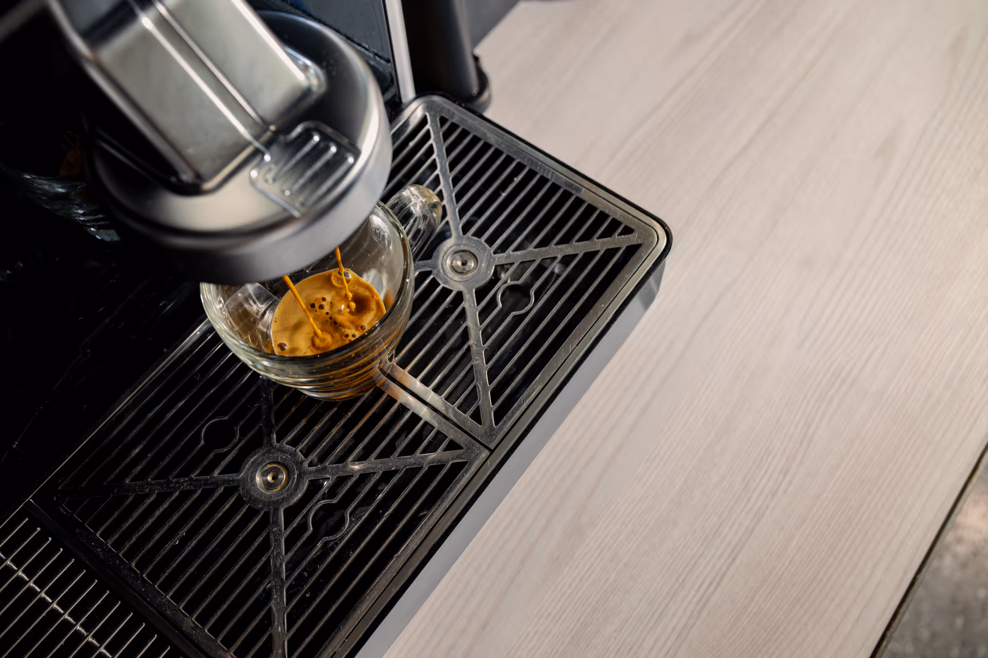 Close-up of espresso machine pouring coffee into a glass cup with crema on top.