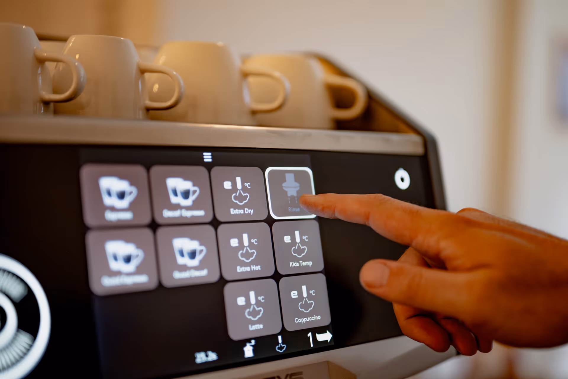 Close-up of a finger pressing the rinse button on a coffee machine touchscreen with cups placed on top.