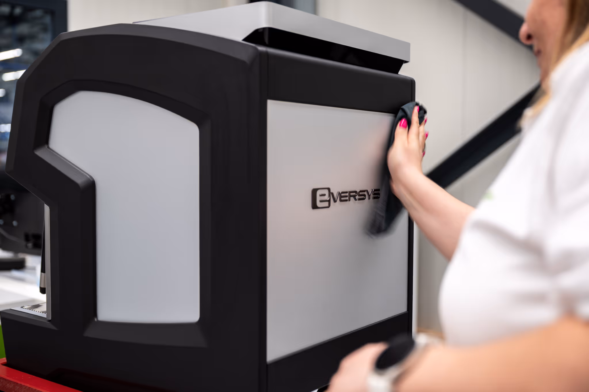Person cleaning the side of a black and gray Eversys coffee machine with a cloth.