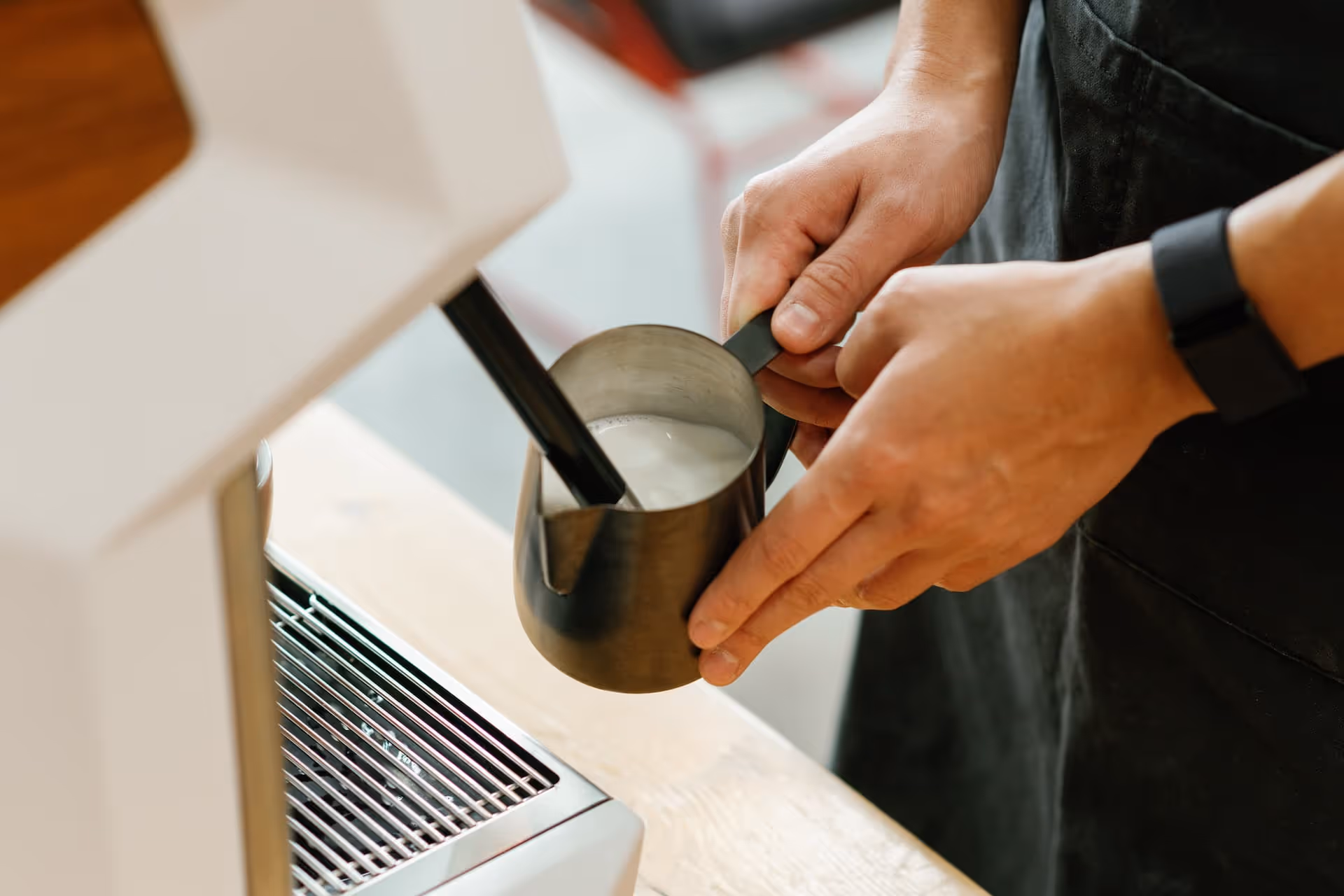 Barista steaming milk in a metal pitcher using an espresso machine steam wand.