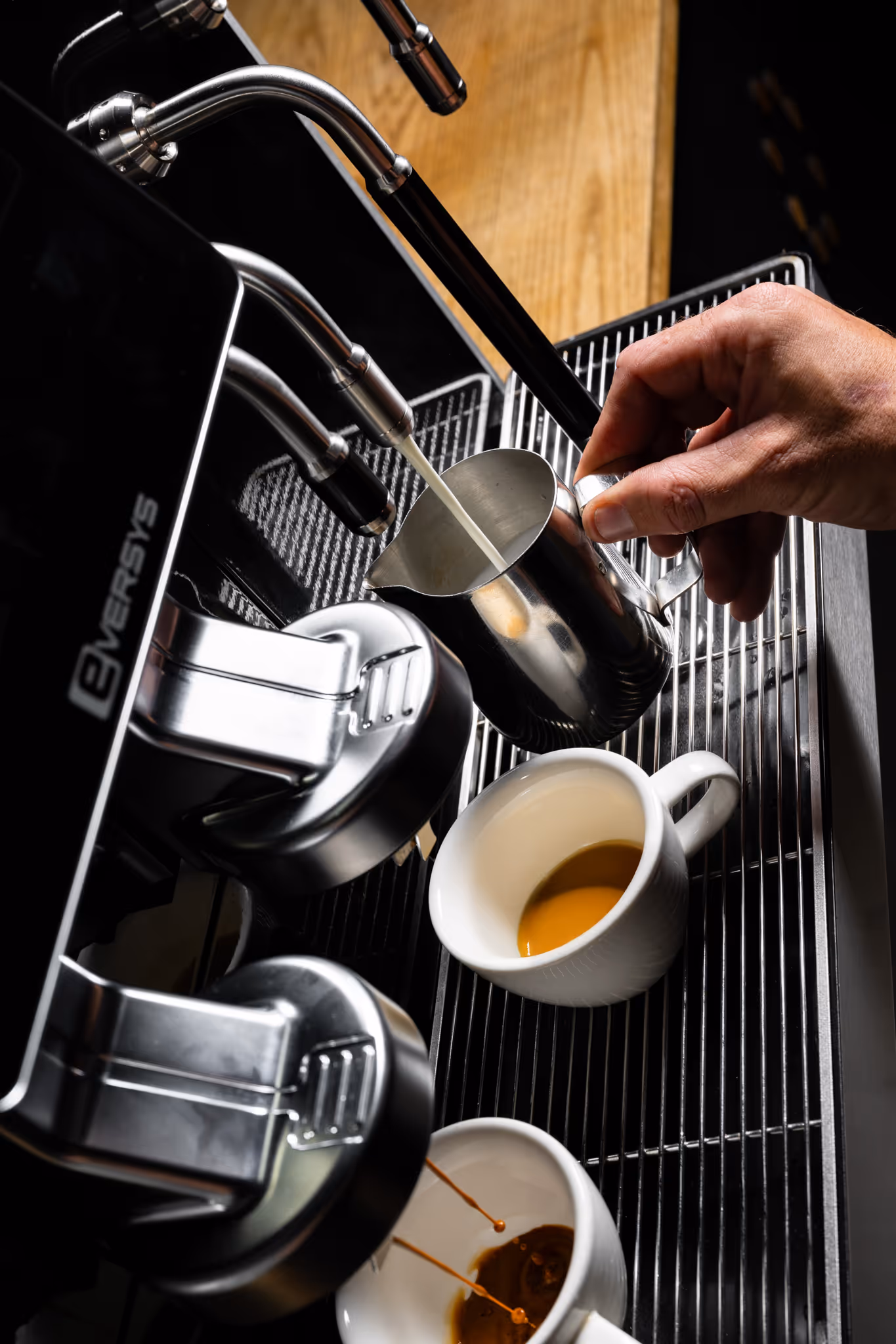 Three black and white espresso cups positioned under a coffee machine with espresso pouring into one cup.