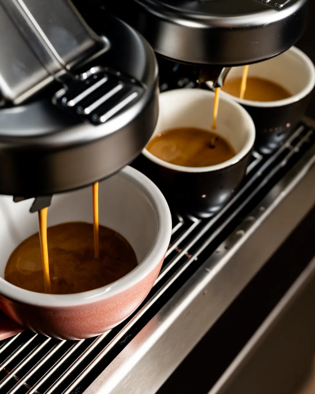 Three espresso cups placed under a coffee machine with espresso brewing.