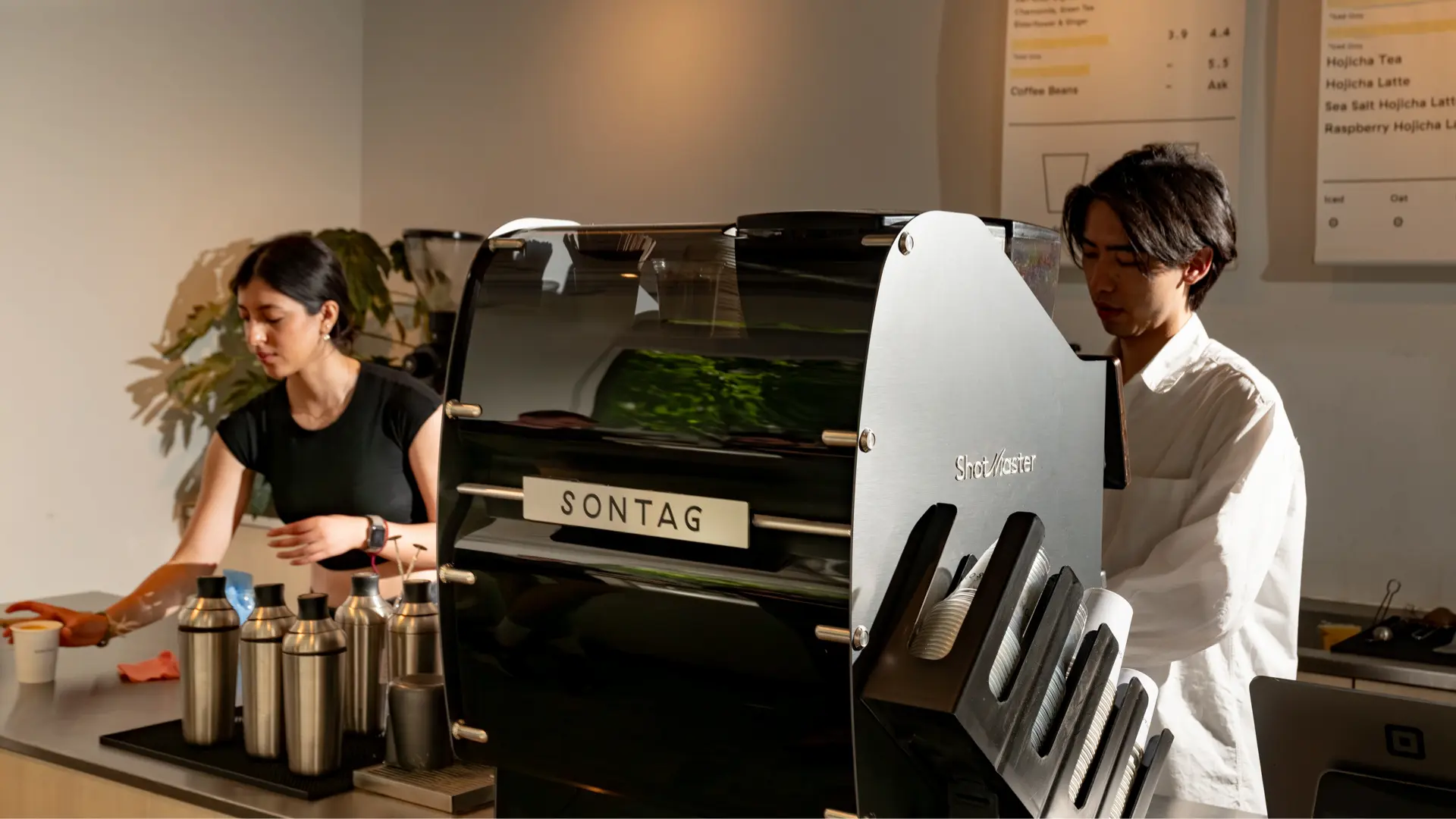 Barista preparing coffee with an espresso machine pouring into a paper cup on a counter with stacked cups nearby.