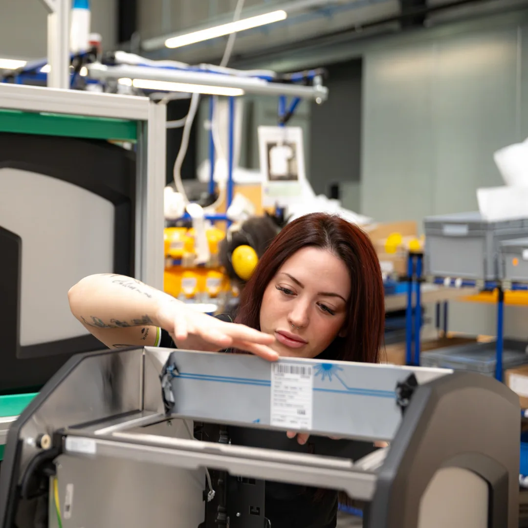 Barista preparing coffee with an automated espresso machine dispensing into a paper cup and a metal pitcher.