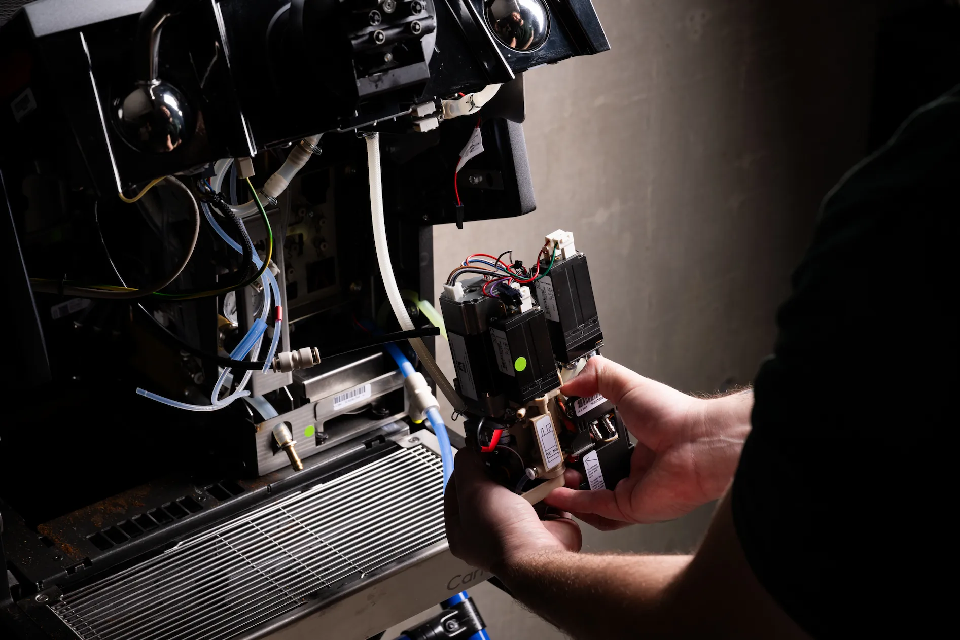 Hands repairing an exposed mechanical and electrical component of a machine with visible wires and tubes.