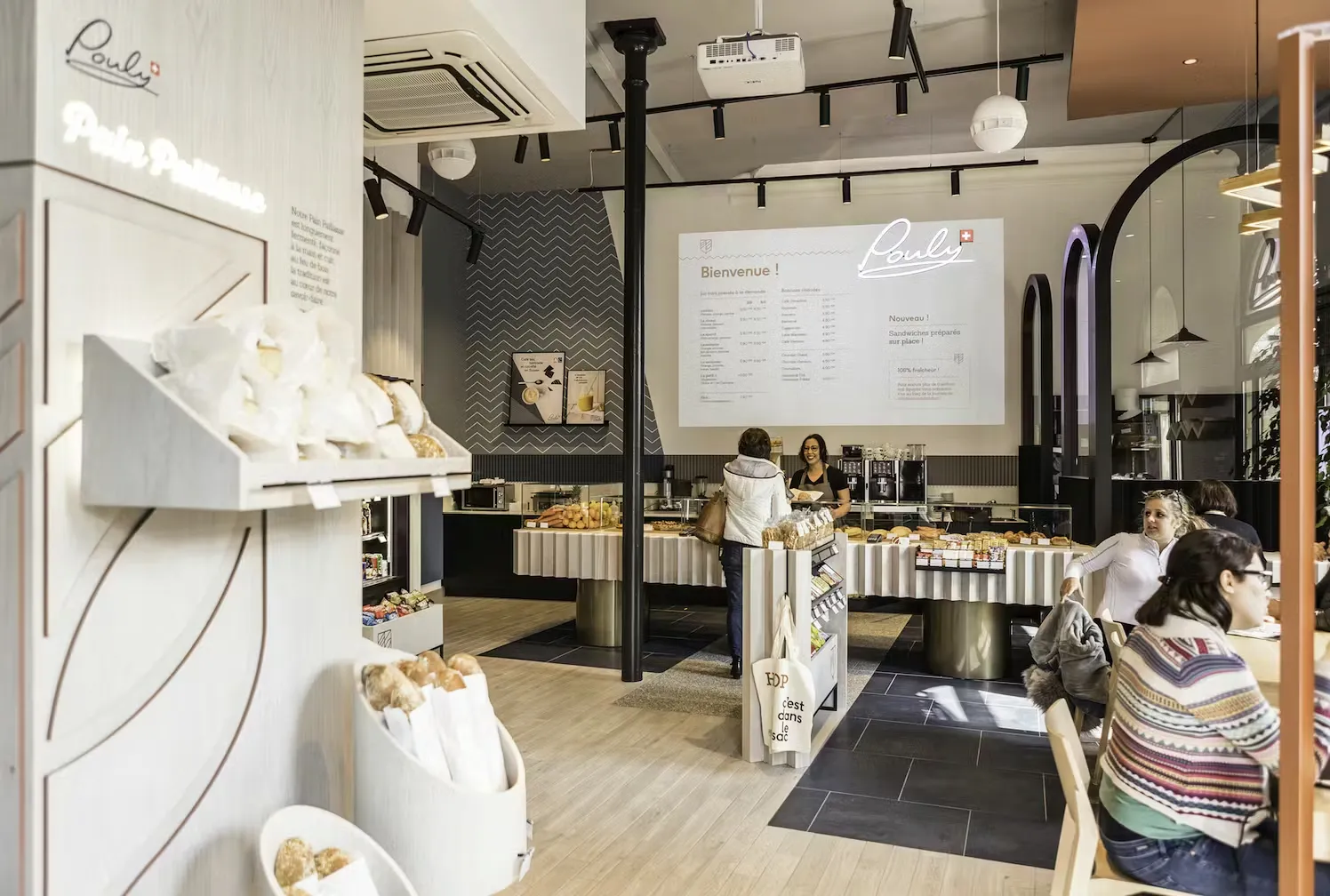 Modern coffee machine and grinder on a counter behind a glass display case filled with assorted pastries in a café.