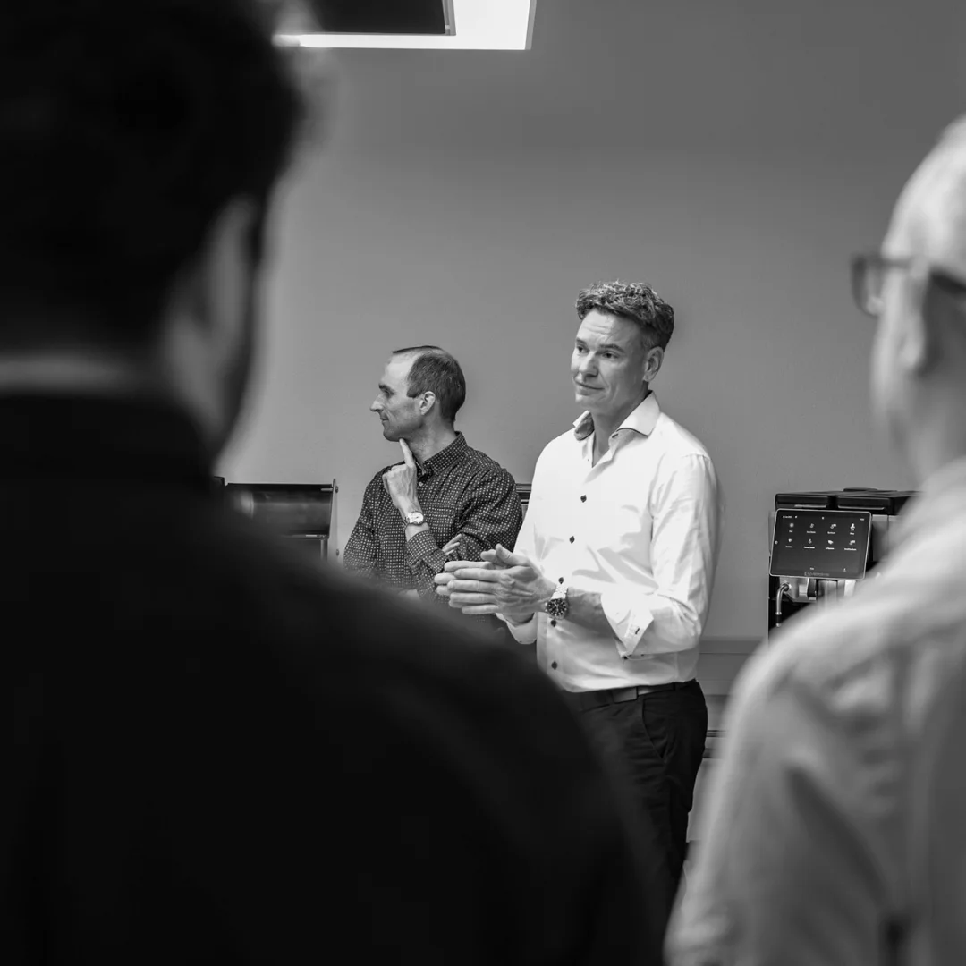 Barista preparing coffee with an automated espresso machine dispensing into a paper cup and a metal pitcher.