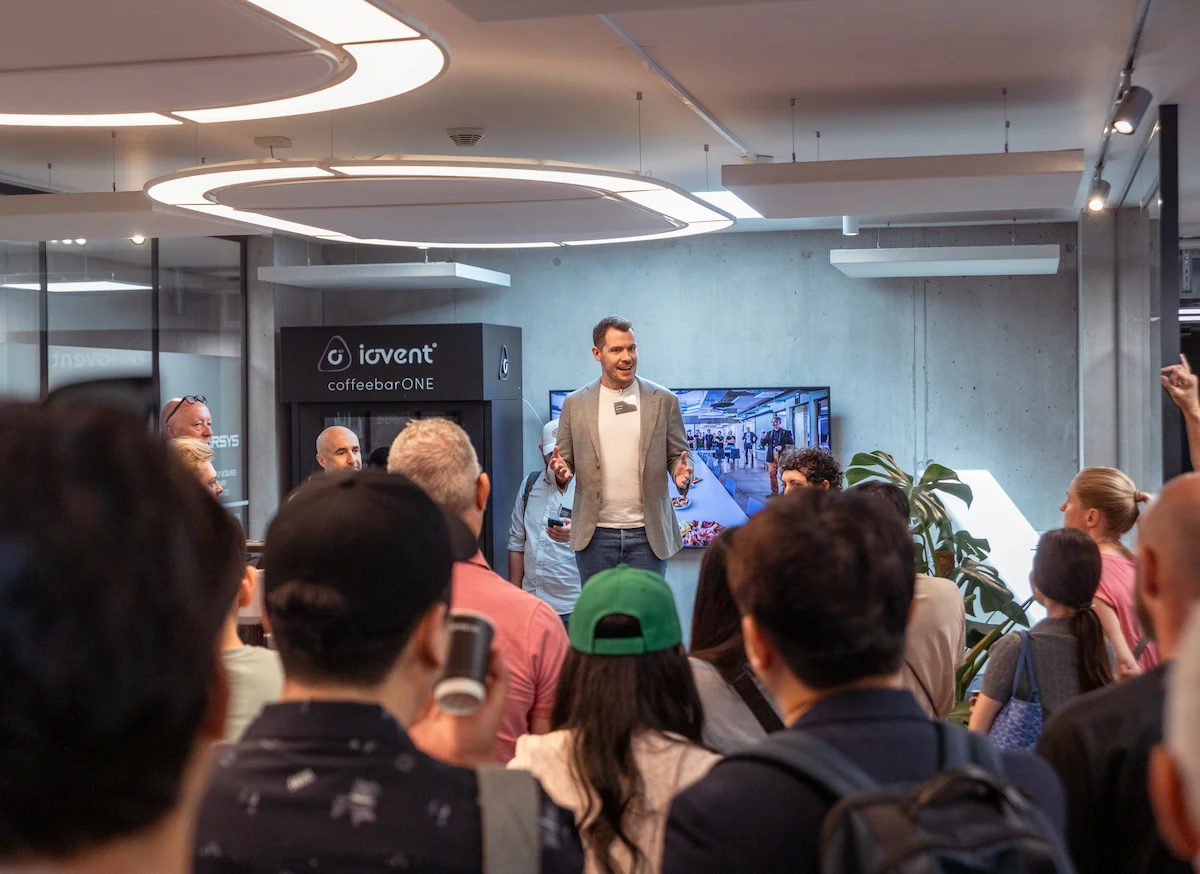 Barista preparing coffee with an automated espresso machine dispensing into a paper cup and a metal pitcher.