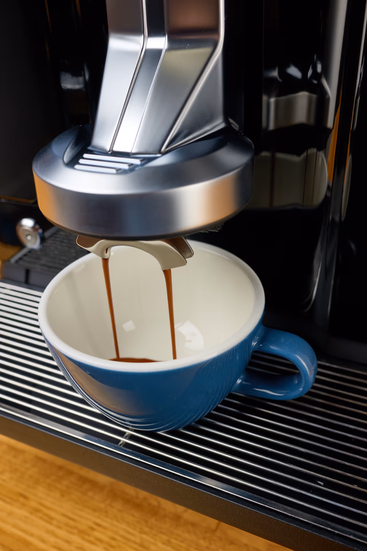 Close-up of espresso machine pouring coffee into a blue ceramic cup on a metal drip tray.