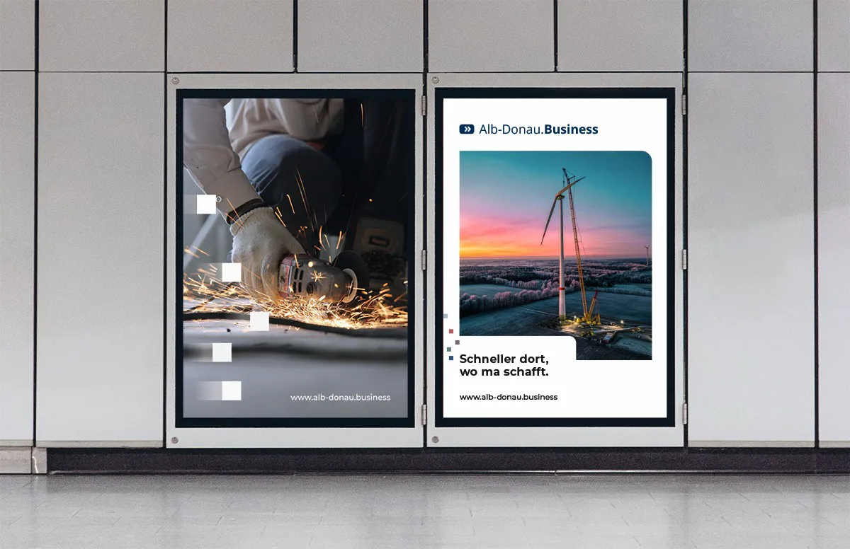 Zwei Werbetafeln in einer Wand: Links ein Bild einer Person, die mit Handschuhen Metall mit einem Schleifgerät bearbeitet, rechts eine Windkraftanlage bei Sonnenuntergang mit dem Text Alb-Donau.Business und „Schneller dort, wo ma schafft.“