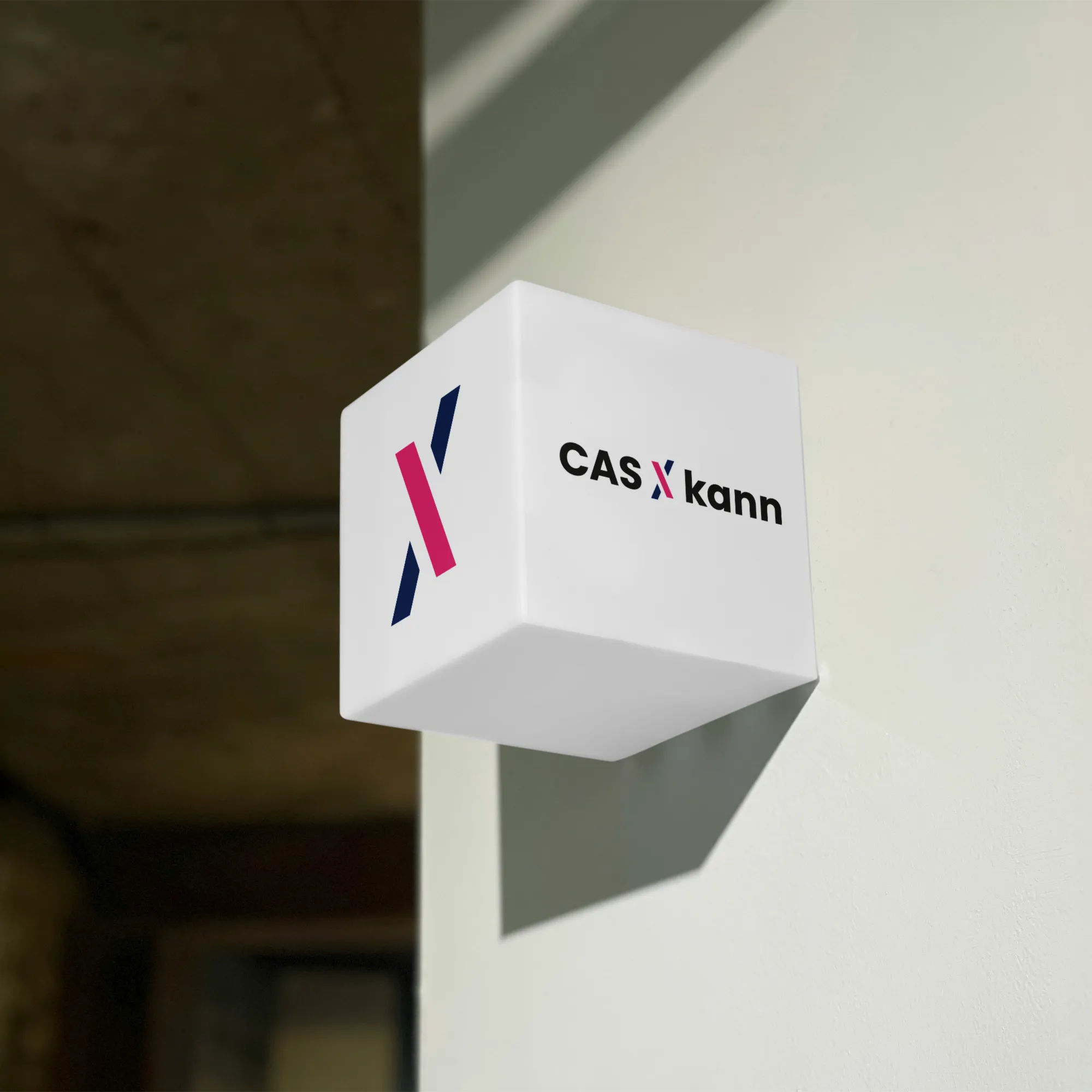 Würfelförmiges Leuchtschild an einer Wand mit einer Grafik aus blauen und roten geometrischen Formen und dem Text ‚CAS X kann‘.