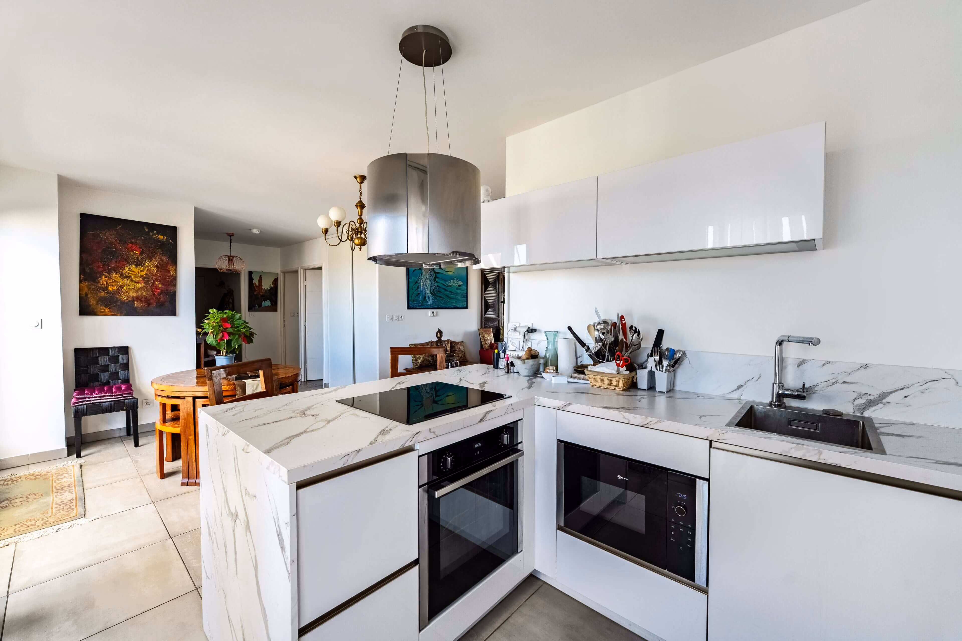 Cuisine moderne blanche avec plan de travail en marbre, four, micro-ondes, table en bois et chaises.