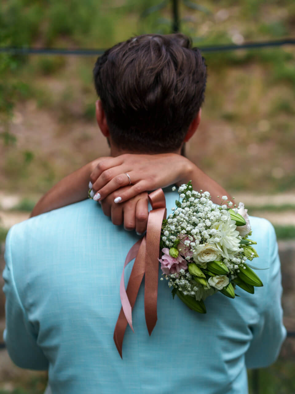 Un homme vu de dos avec une femme tenant un bouquet de fleurs blanches et une bague de fiançailles.