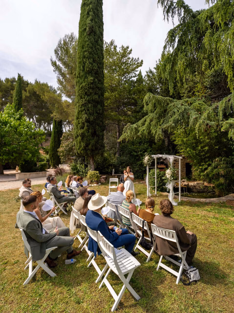 Petite cérémonie de mariage en plein air avec invités assis sur des chaises blanches dans un jardin.