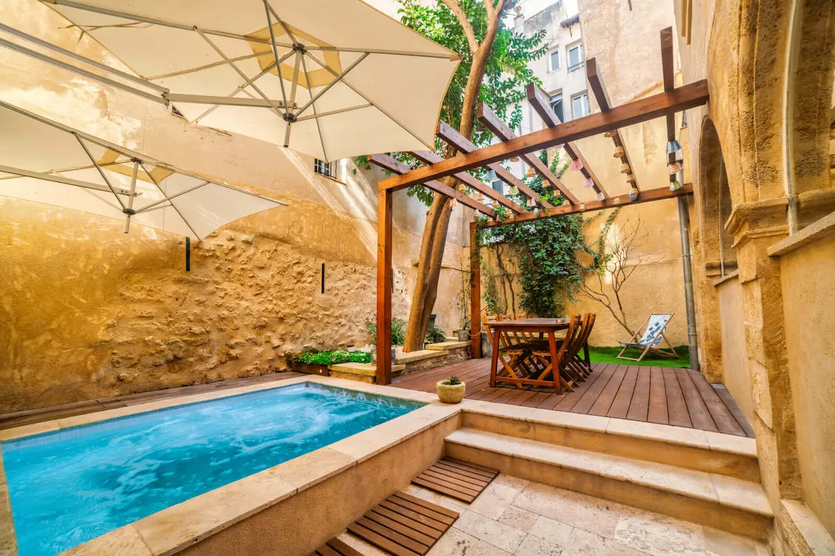 Terrasse extérieure avec piscine, parasols, pergola en bois et table à manger avec chaises en ville.
