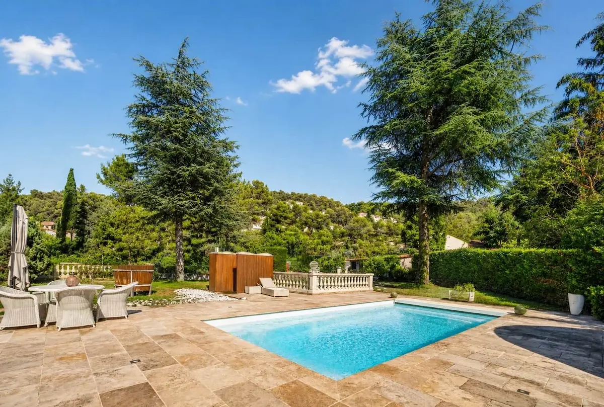 Piscine extérieure entourée de grandes arbres et meubles de jardin sous un ciel dégagé.