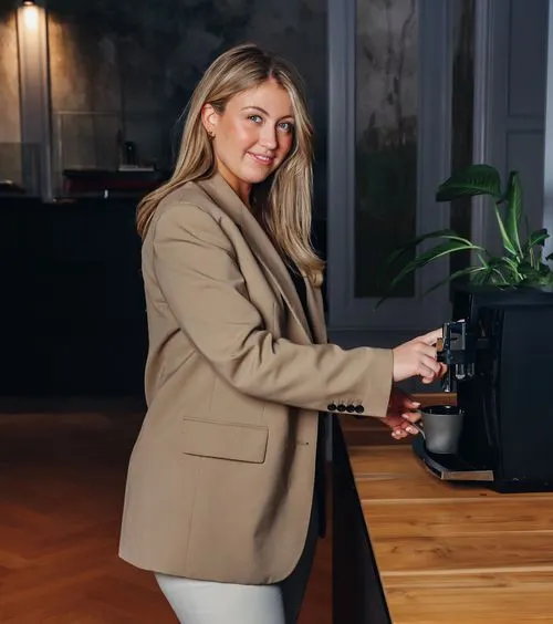 Mujer sonriendo mientras prepara café con una máquina de café en una cocina moderna.