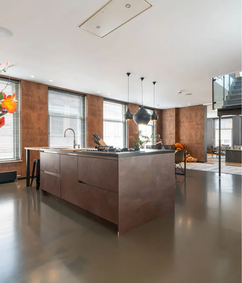 Cocina moderna con isla central marrón, lámparas colgantes negras y grandes ventanas con persianas.