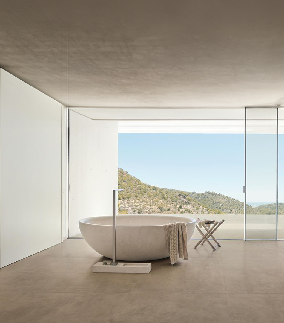 Baño moderno con bañera independiente blanca frente a ventana panorámica que muestra colinas verdes bajo cielo azul.