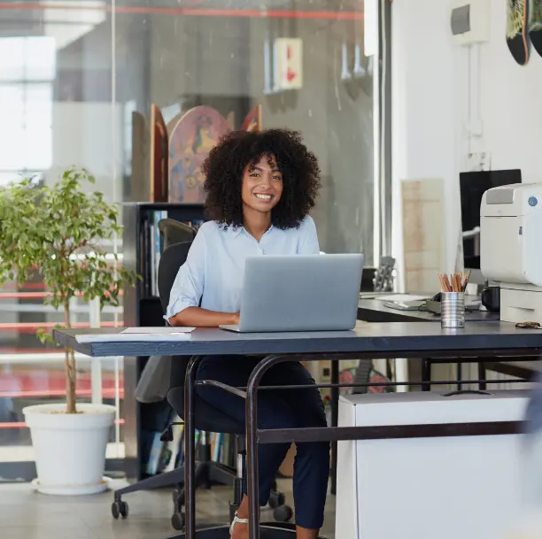 Femme souriante travaillant sur un ordinateur portable dans un bureau moderne, symbolisant la confiance et le développement professionnel