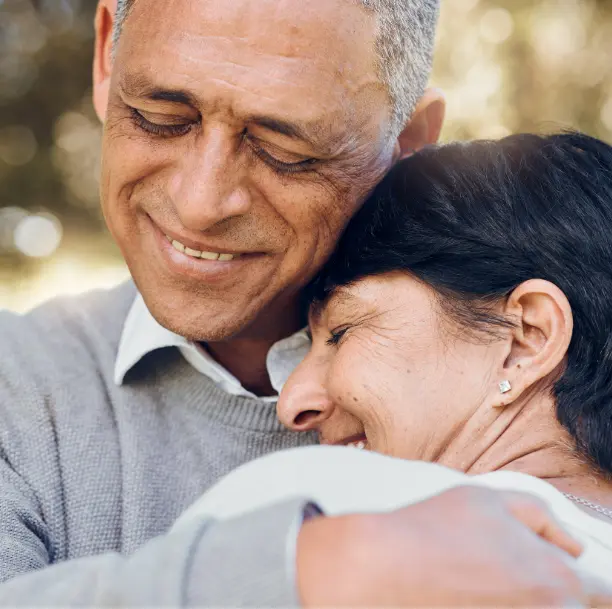Couple senior échangeant un câlin chaleureux avec un sourire, illustrant l’émotion, le réconfort et la confiance