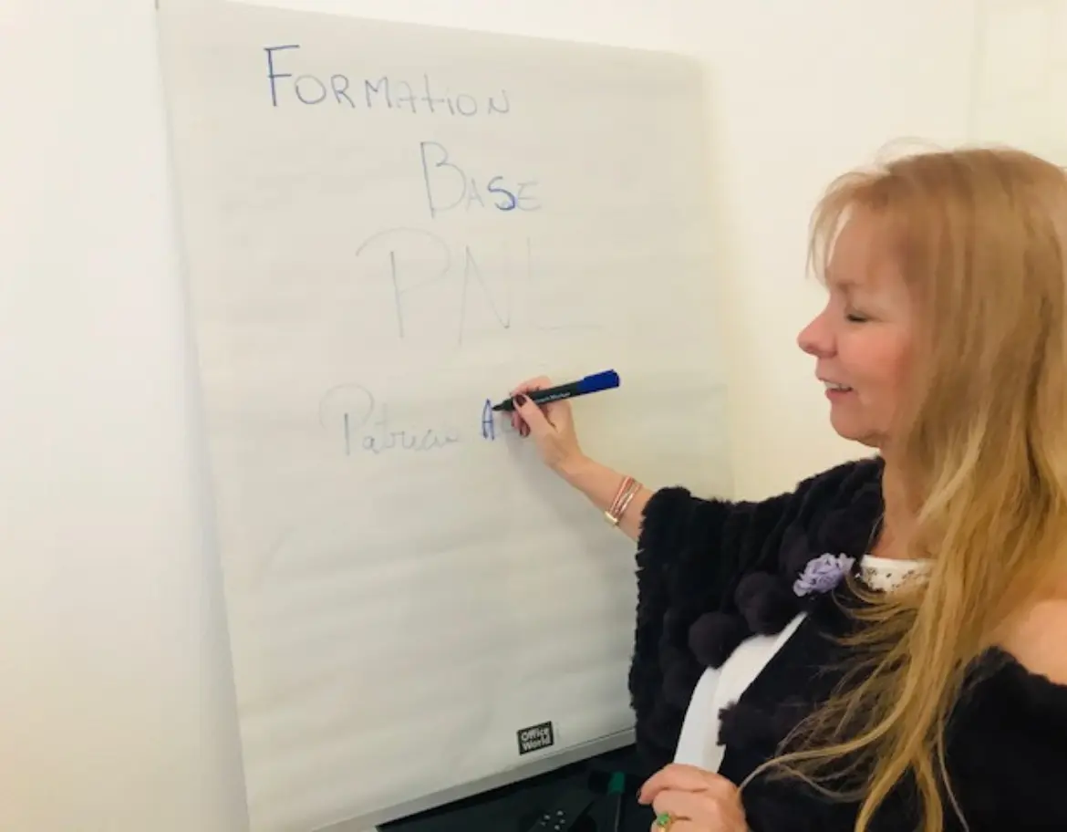 Patricia, formatrice en PNL, expliquant un concept sur un tableau blanc lors d’une séance de formation