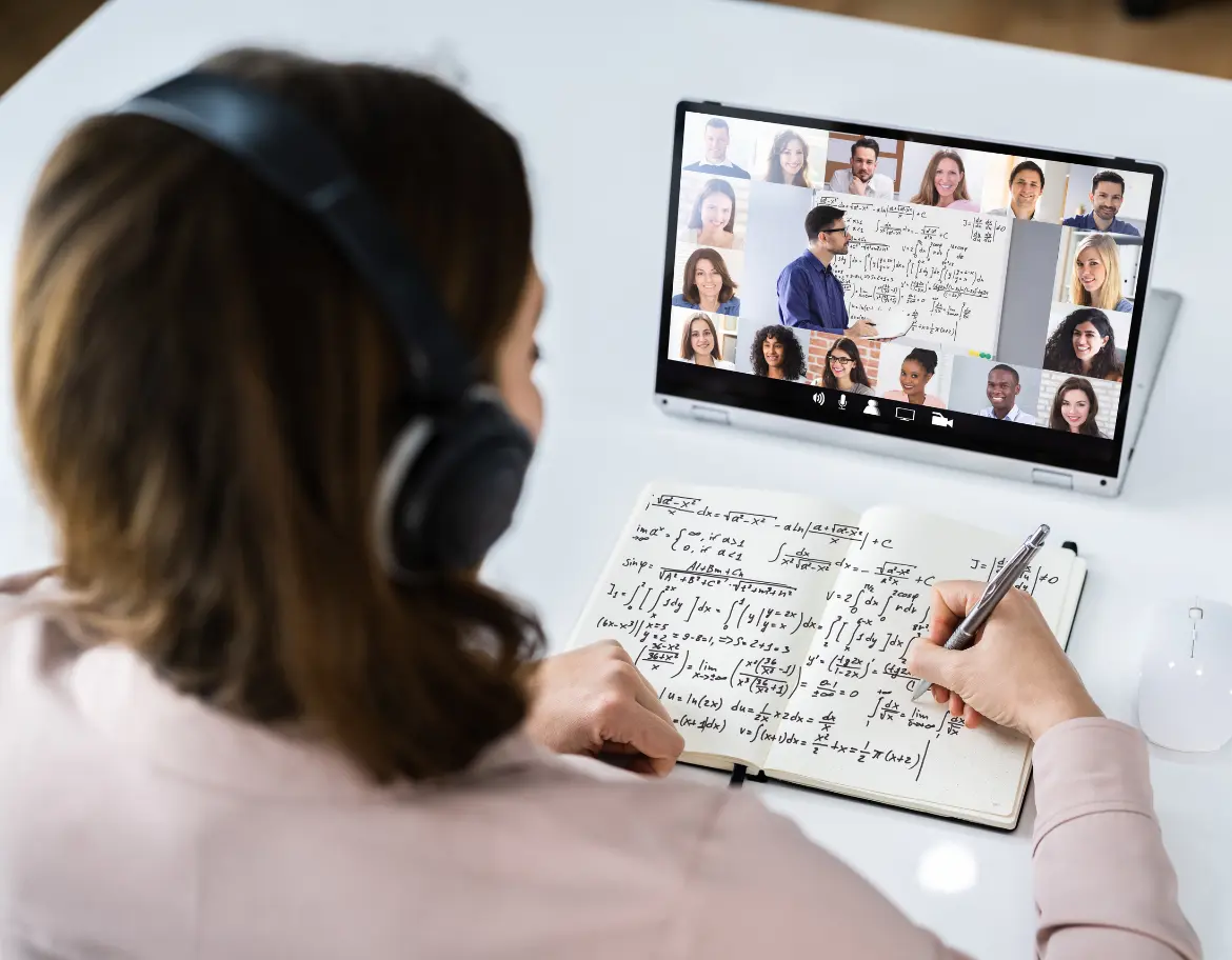 Femme assistant à une formation en ligne en PNL, prenant des notes tout en écoutant un formateur et interagissant avec d’autres participants en visioconférence