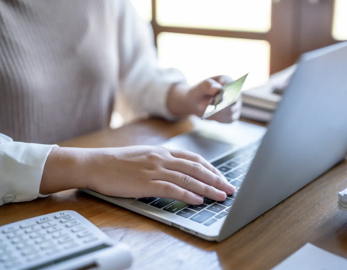Personne effectuant un paiement en ligne pour une formation en PNL, carte bancaire à la main et ordinateur portable ouvert sur une page d'inscription