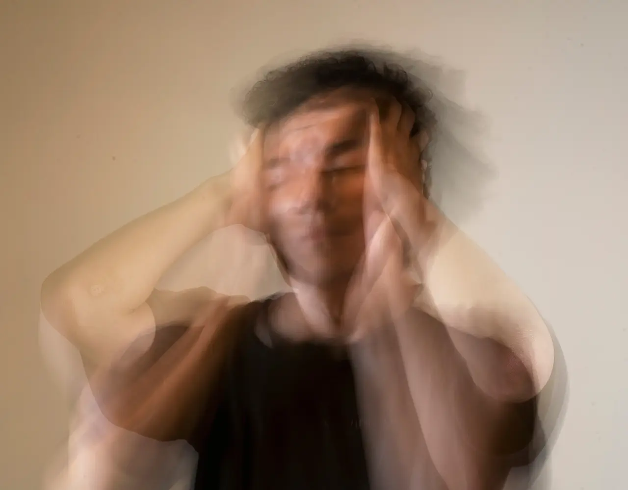 Homme en détresse tenant sa tête avec un effet flou, représentant l’anxiété, la surcharge mentale et les troubles émotionnels