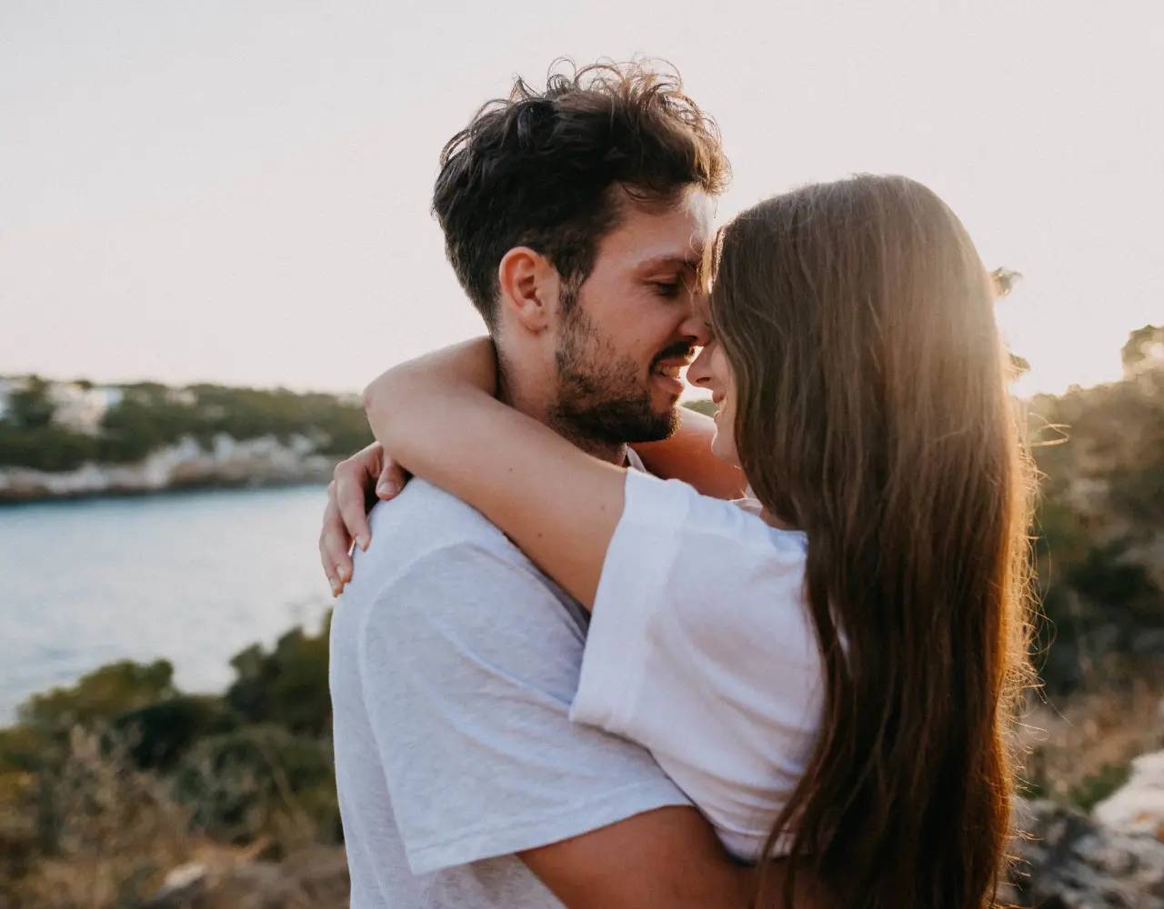 Couple s’enlaçant tendrement au bord de l’eau, illustrant la connexion émotionnelle et l’épanouissement dans la relation