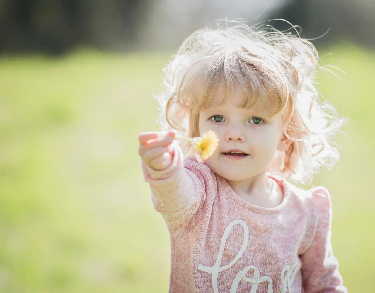 Petite fille souriante tendant une fleur dans un champ ensoleillé, incarnant l’innocence, la générosité et le bien-être de l’enfance