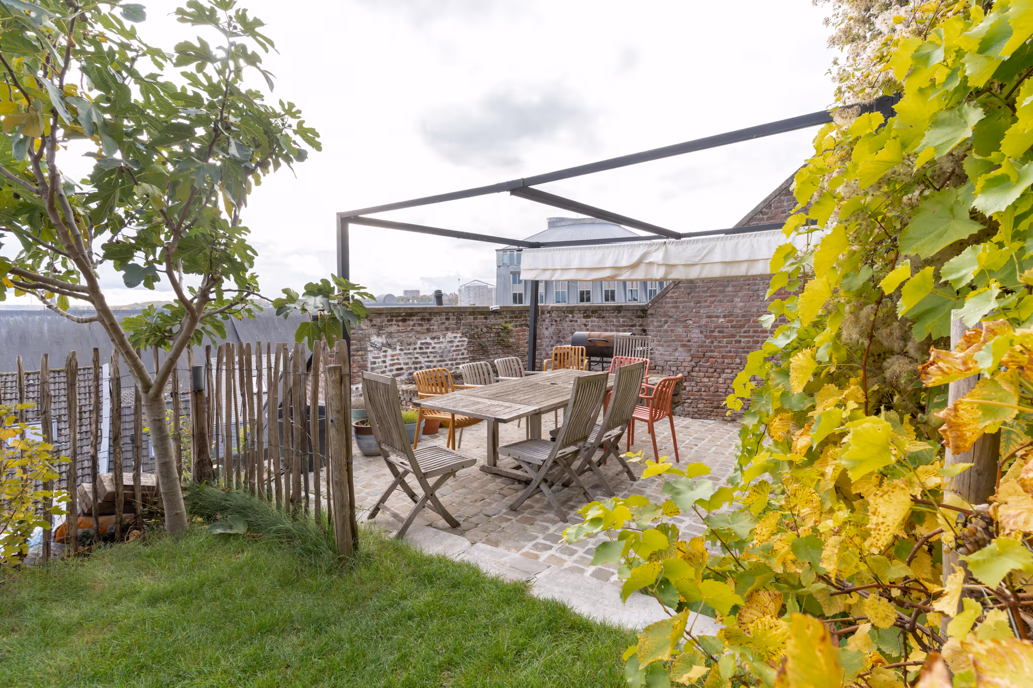 Terrasse urbaine avec table en bois et chaises, entourée de murs en briques, plantes vertes et gazon.