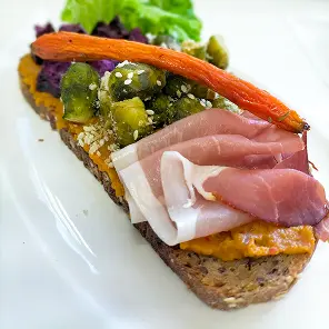 Tartine ouverte sur pain complet garnie de jambon blanc, légumes marinés verts, carotte râpée et salade verte