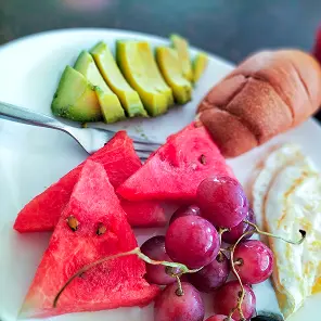 Assiette de fruits frais variés : tranches d'avocat vert, pastèque rouge, raisins roses et banane, disposés de manière colorée
