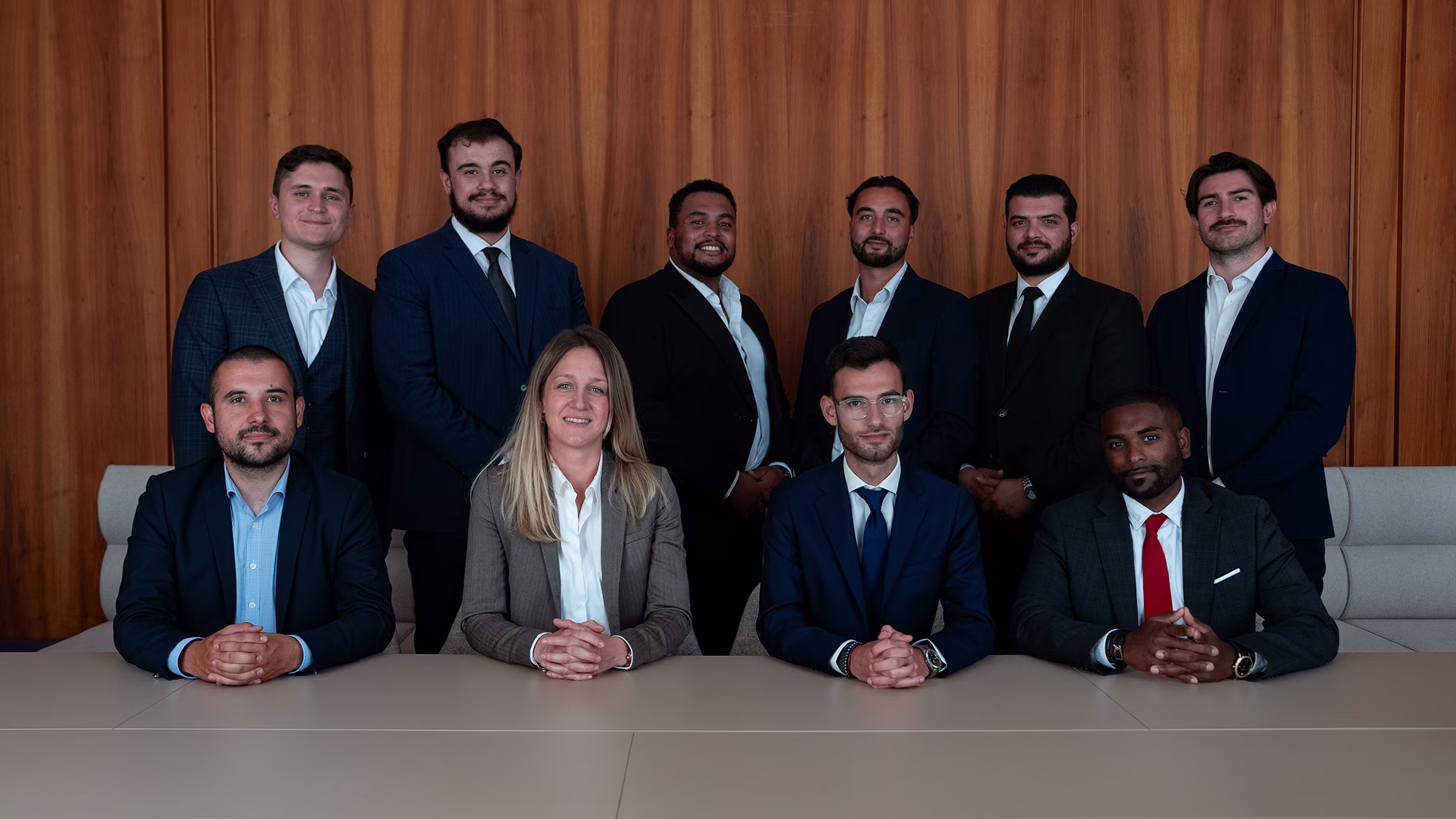 Groupe de dix professionnels en tenue formelle posant assis et debout devant un mur en bois.