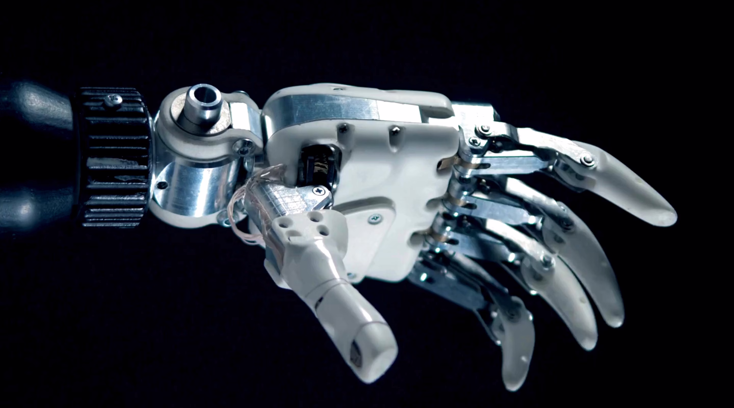 Main robotique articulée en métal et plastique sur fond noir.