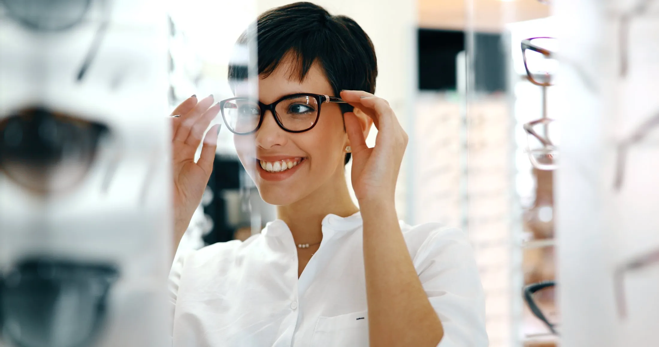 Smiling woman trying on glasses in optical store with blurred background