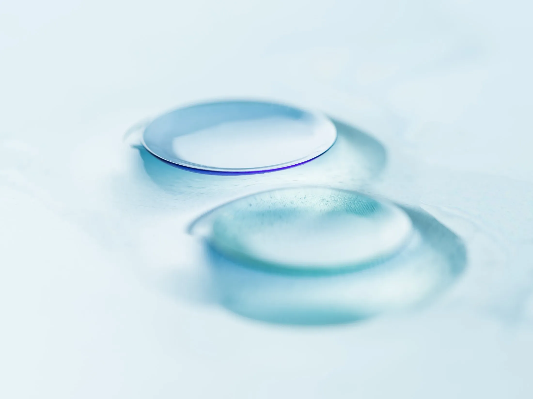 Two translucent blue glass or contact lenses on soft blue background