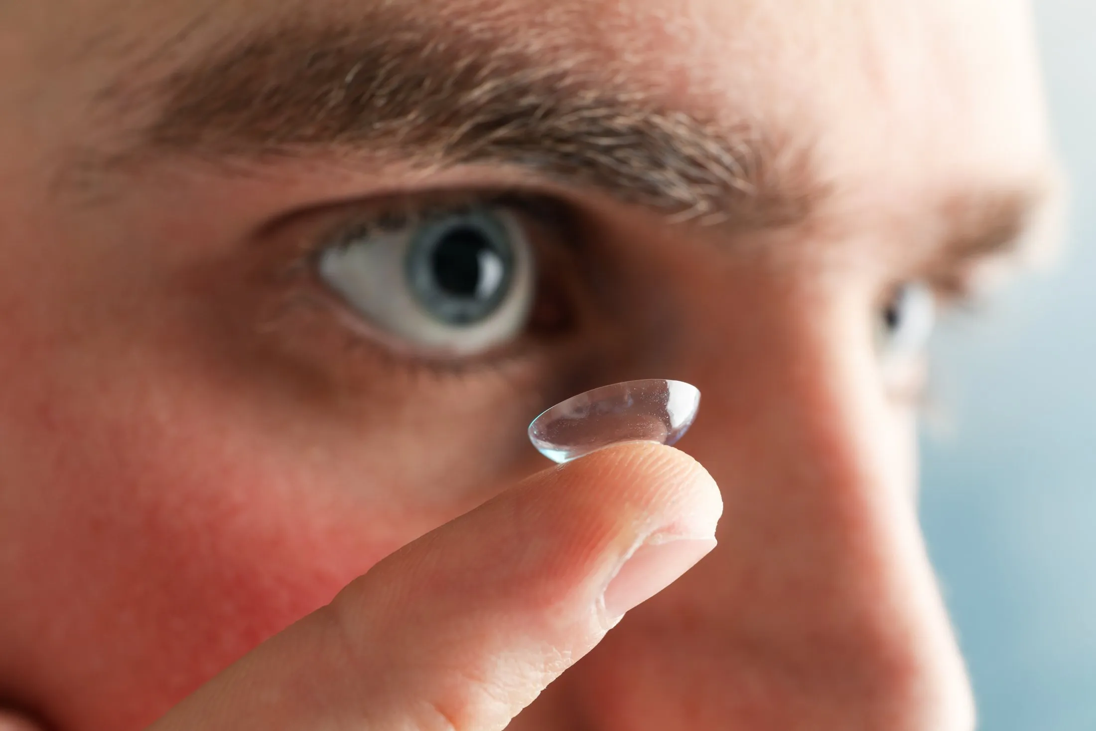 Close-up of contact lens on finger near eye with blurred background