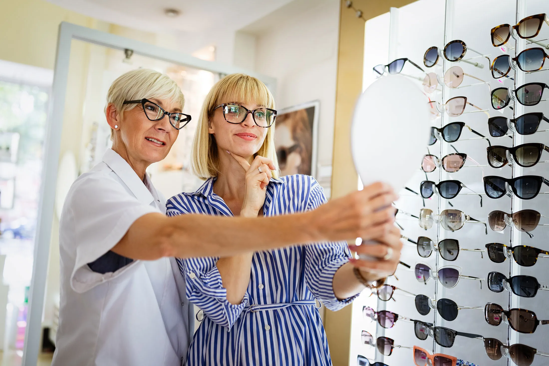 Two women selecting sunglasses in an optical store display