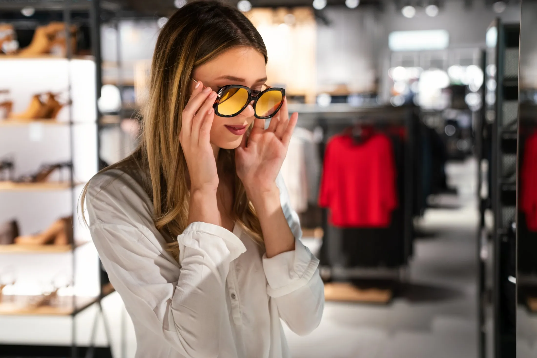 Woman trying on yellow-tinted sunglasses in a clothing store