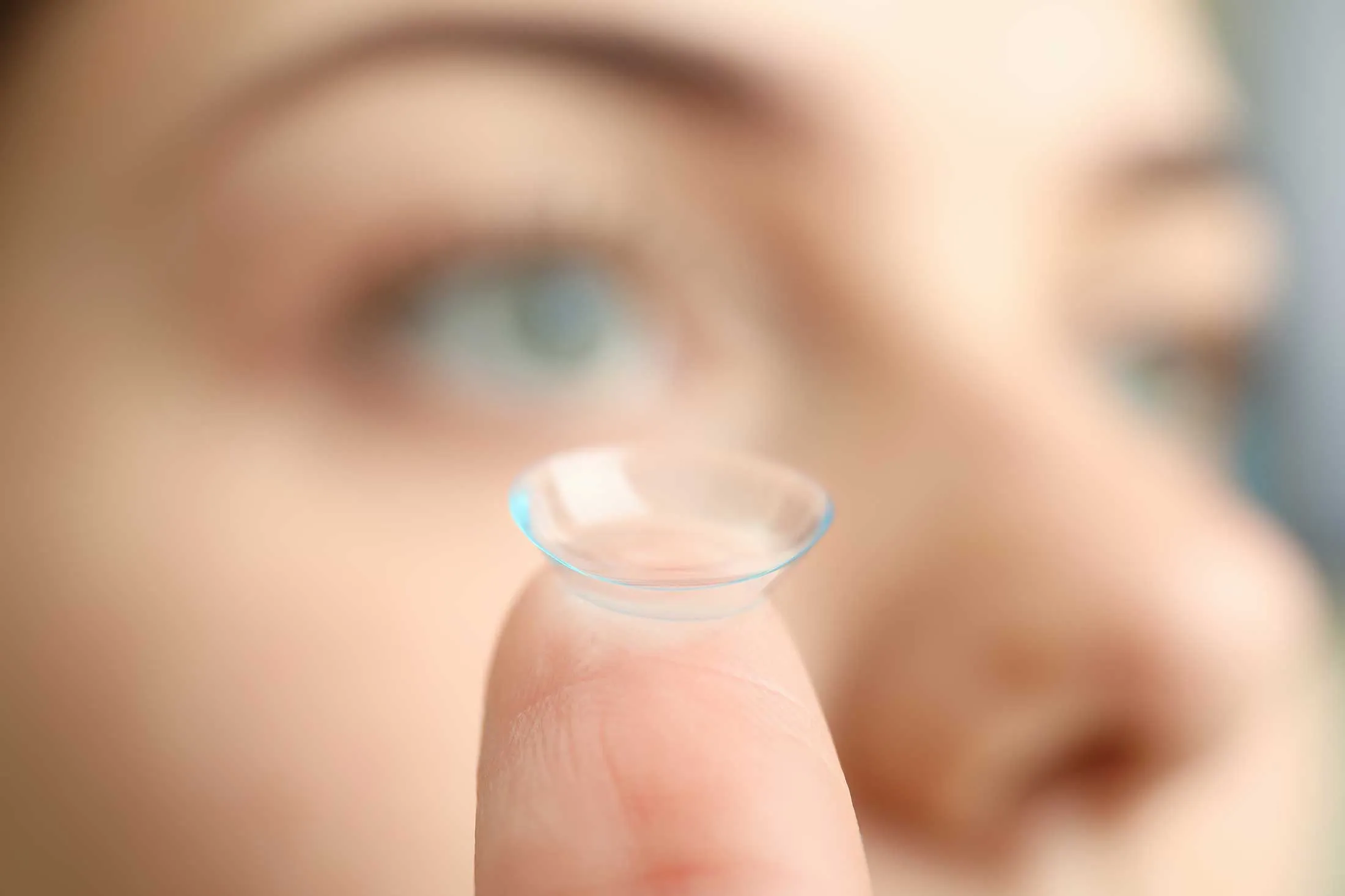 Transparent contact lens balanced on fingertip near blurry face