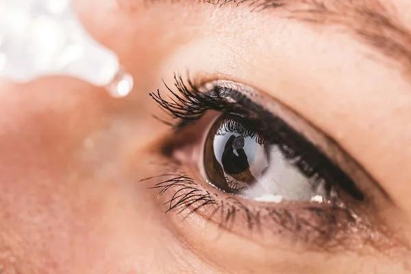 Close-up of human eye with long eyelashes and eye drop applying