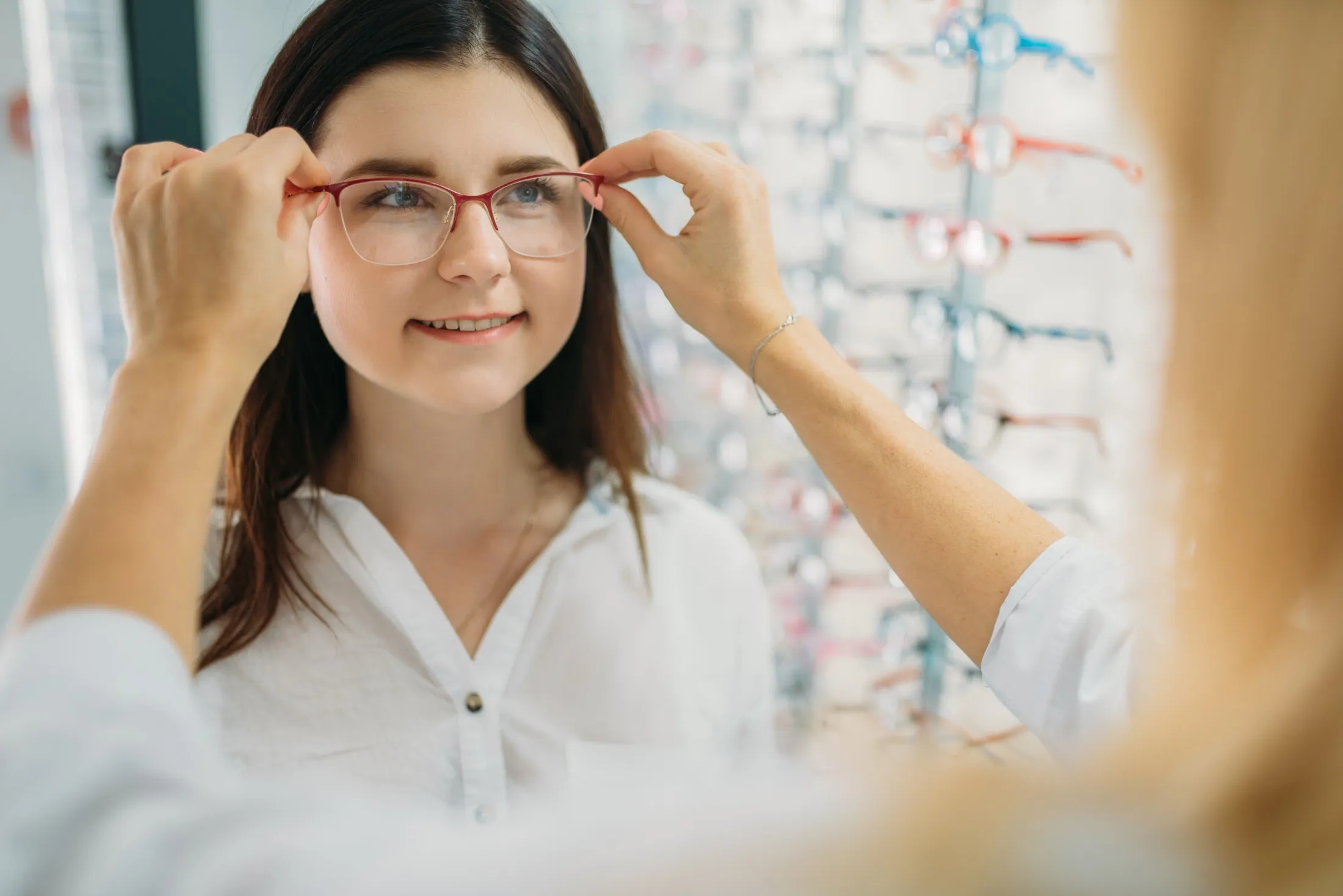 Person trying on red-framed glasses in optical store with display background