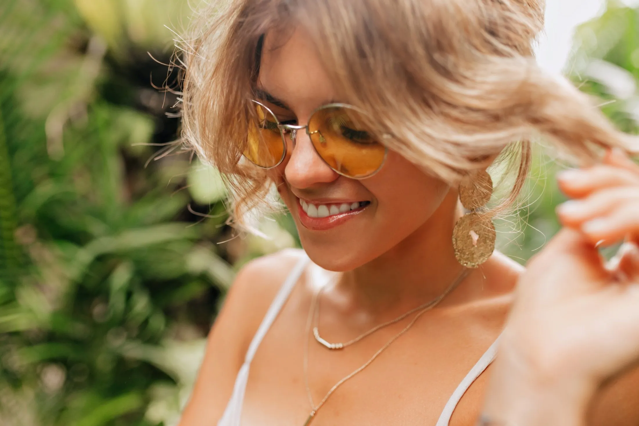 Smiling woman with yellow sunglasses and wavy hair in green outdoor setting