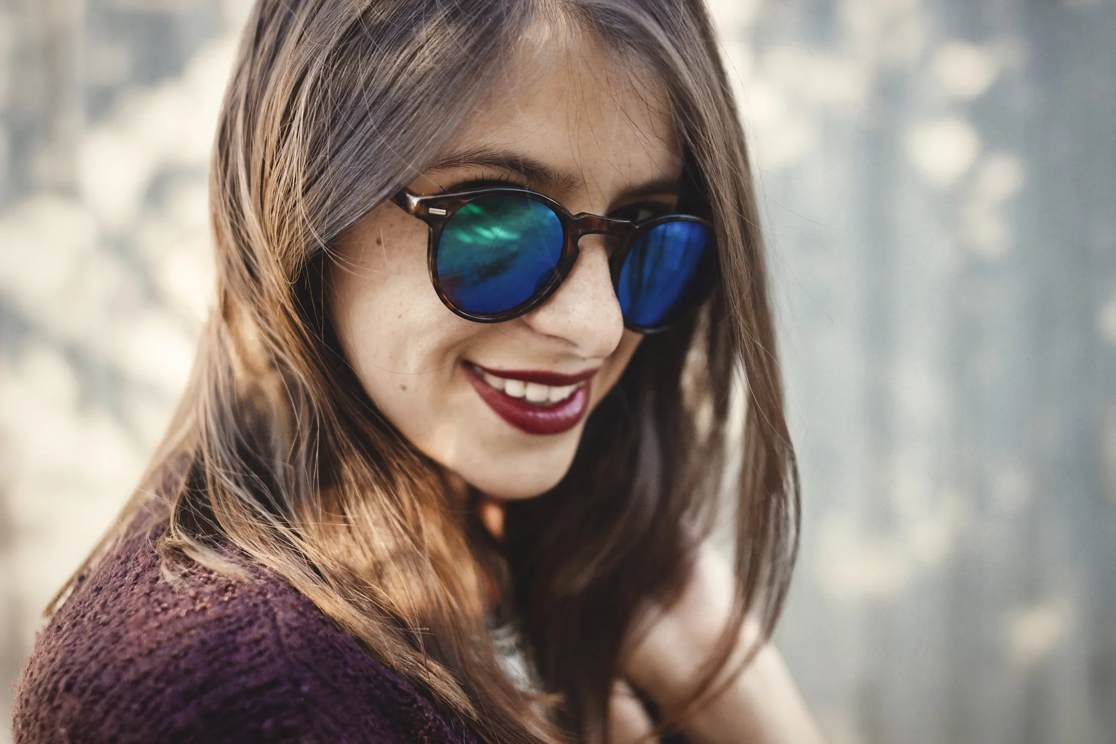 Smiling woman wearing blue-green mirrored sunglasses and purple sweater