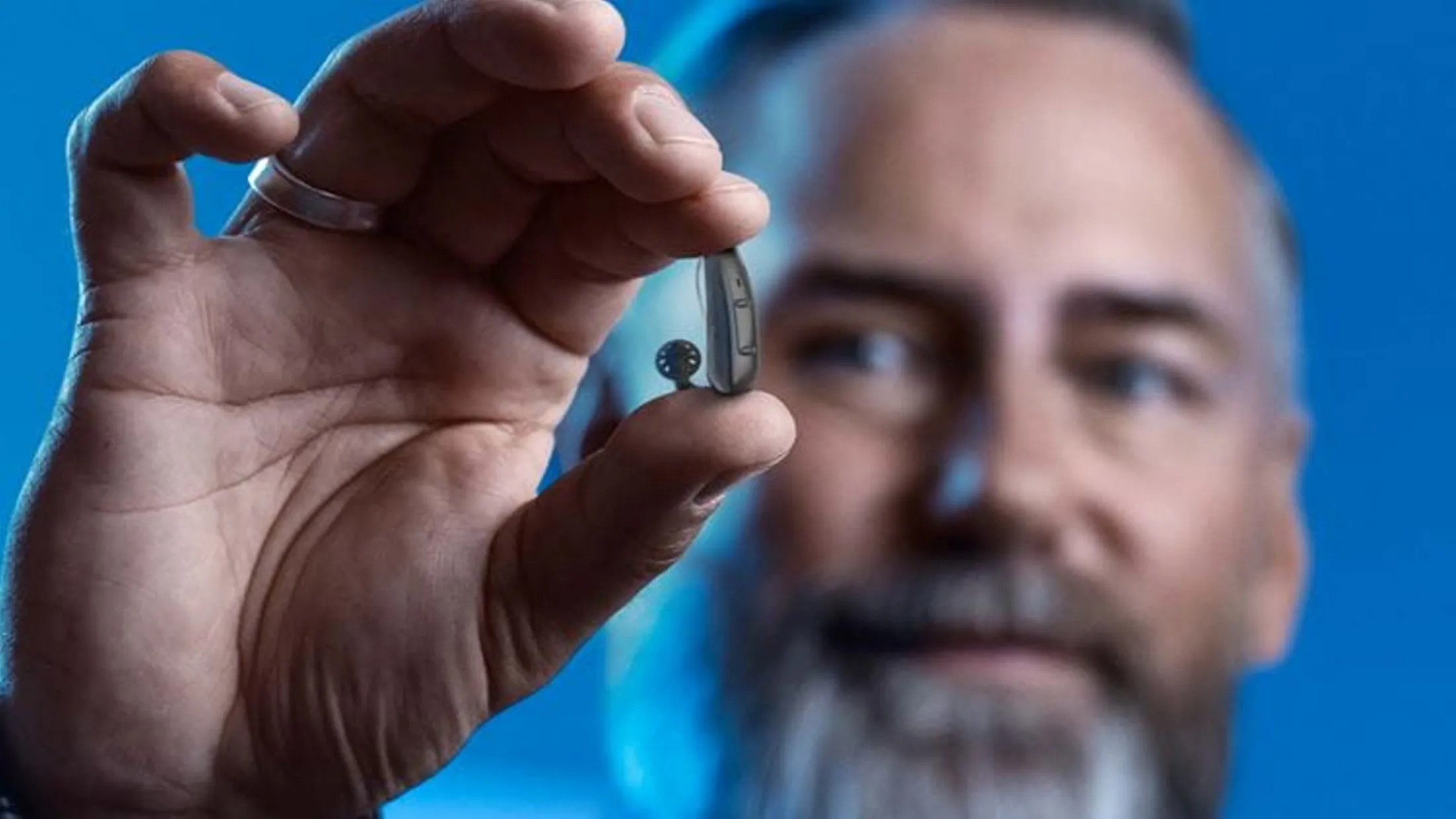 Person holding small hearing aid device against blue background