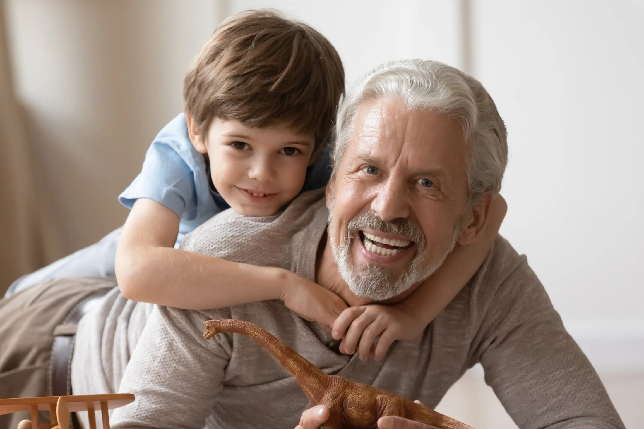 Grandfather and grandson smiling together, holding a dinosaur toy