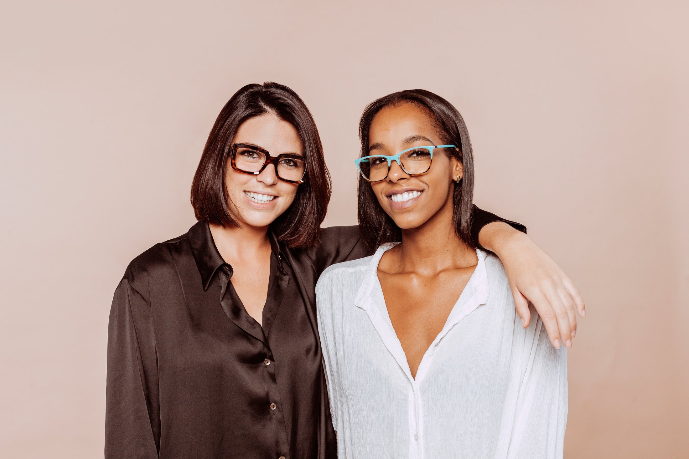 Two smiling women in glasses, one in black, one in white shirt