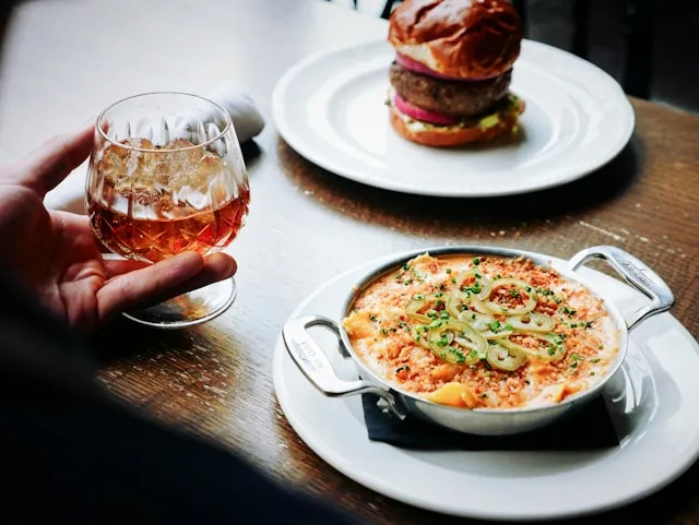 A person holding a glass of wine in front of a plate of food.